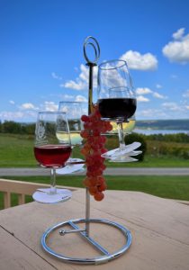 Three filled wine glasses and a bunch of red grapes hanging from a display on the deck table